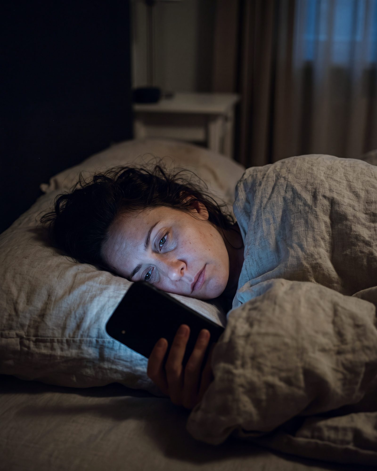 1 h du matin, une femme dans son lit, le visage éclairé en bleu par son téléphone