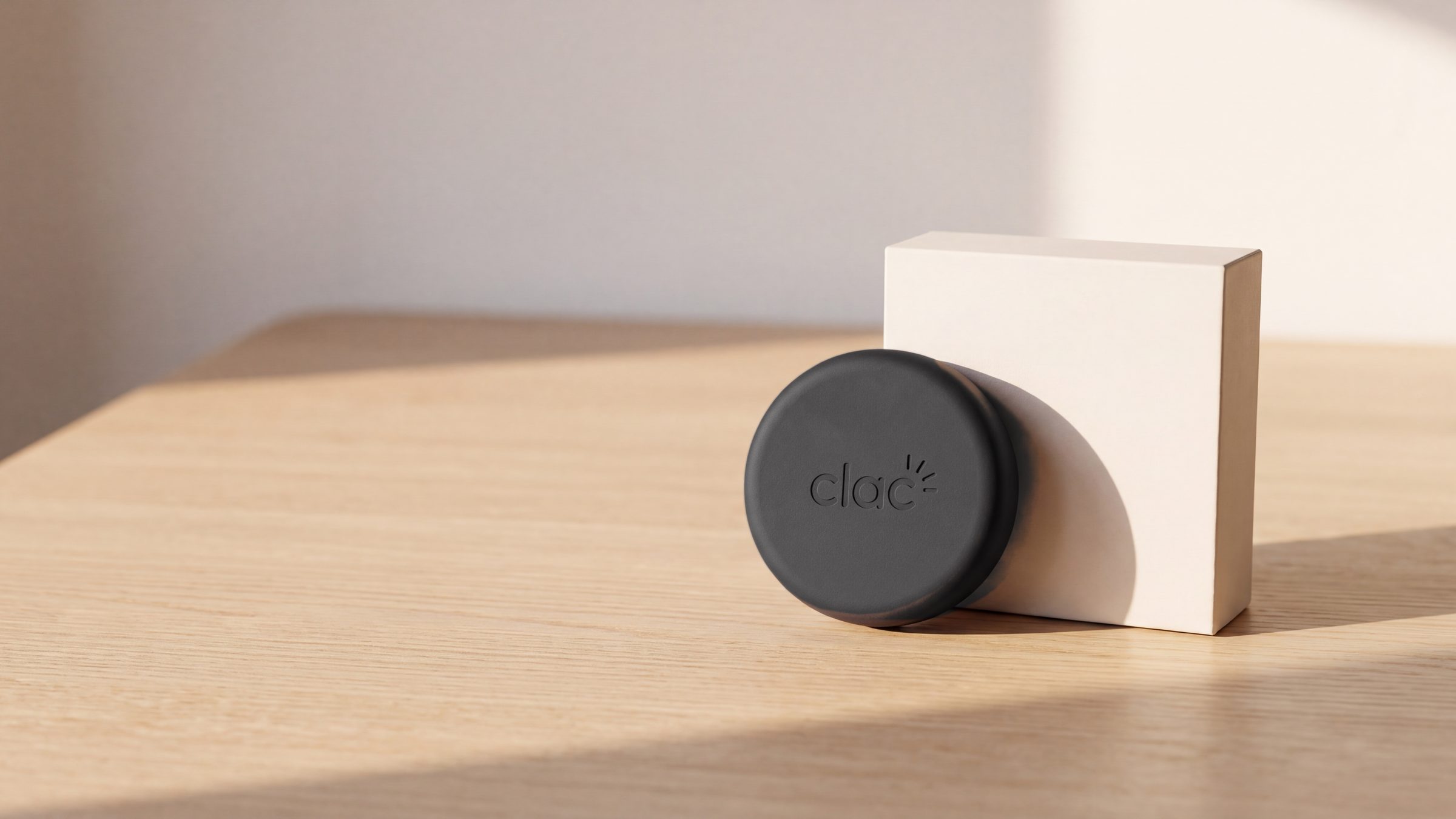 Le Clac et sa boîte blanche sur une table en bois clair, dans une lumière chaude